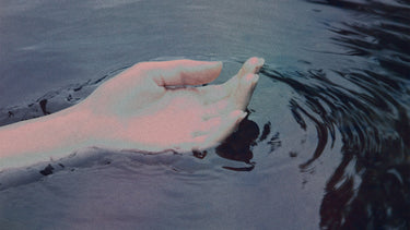 #A serene image of a hand gently touching the water, creating ripples, symbolizing calmness and connection with nature